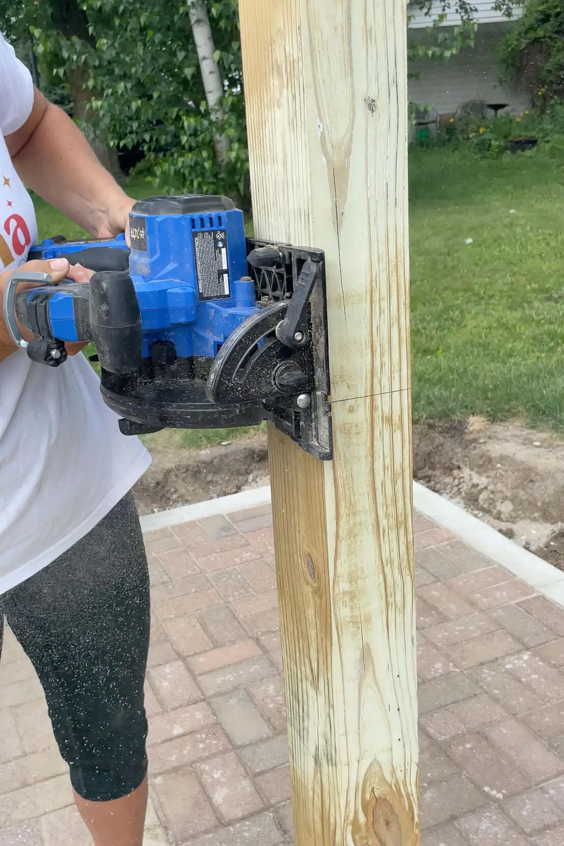 Woman using a circular saw to cut a wood post to the correct height while building a DIY privacy fence.